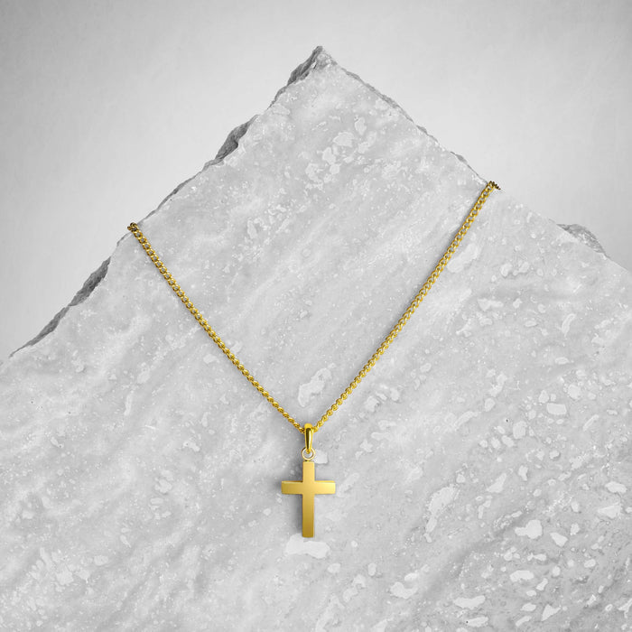 Gold cross necklace on a textured gray surface