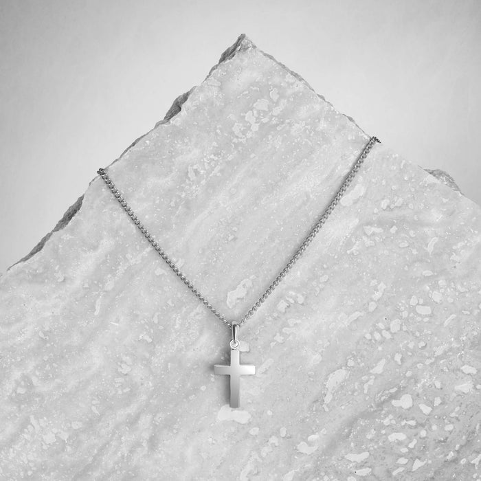 Silver cross necklace on a textured gray surface