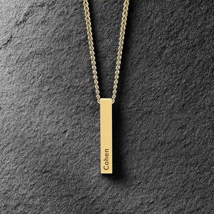 Gold necklace with a vertical bar pendant on a dark stone background