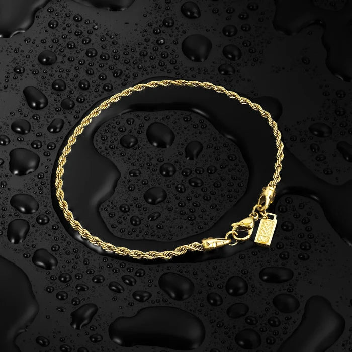 Gold bracelet with a pendant on a black textured surface with water droplets