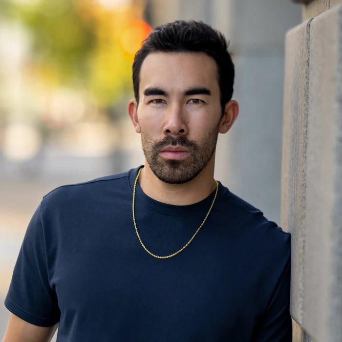 Man wearing a navy blue t-shirt with a gold chain, standing outdoors.