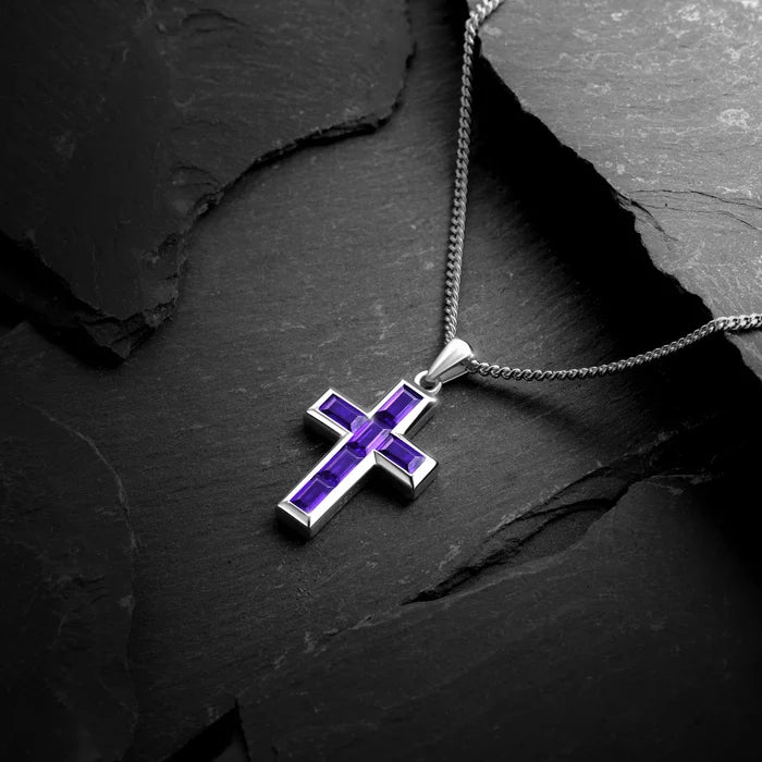 Silver cross pendant with purple accents on a dark stone surface