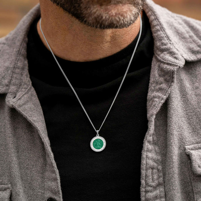 Man wearing a gray jacket over a black shirt with a silver necklace featuring a green pendant.