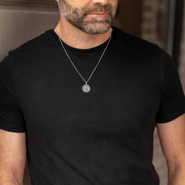 Man wearing a black t-shirt and silver necklace with a pendant.