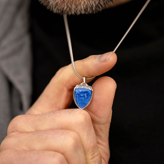Hand holding a necklace with a blue pendant against a dark background