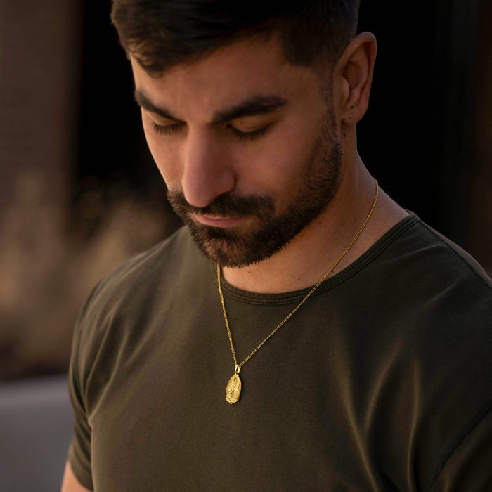 Man wearing a gold necklace with a pendant against a blurred background