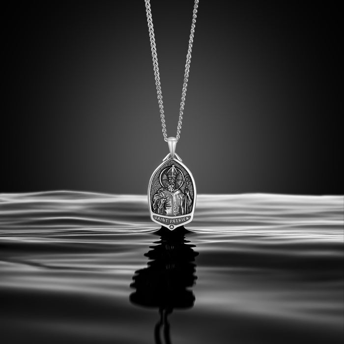 Silver pendant necklace with intricate design on a reflective surface