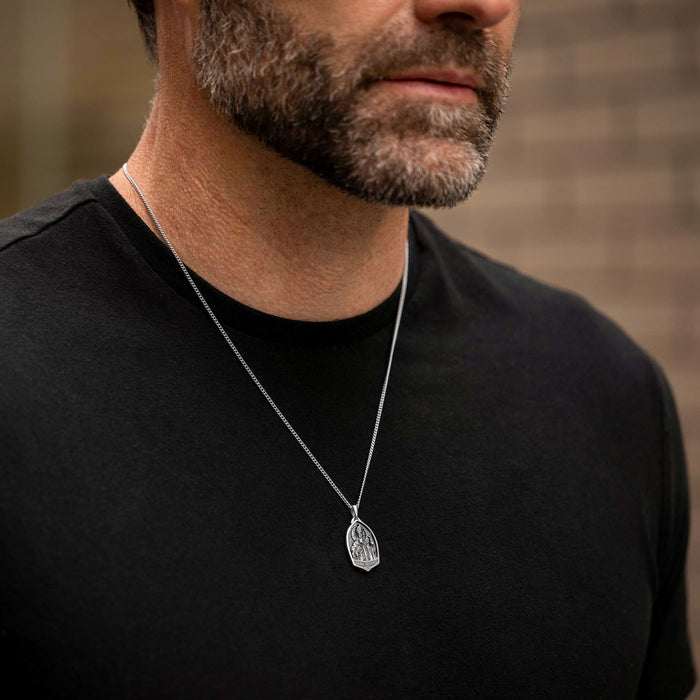 Man wearing a black shirt with a silver necklace featuring a pendant.