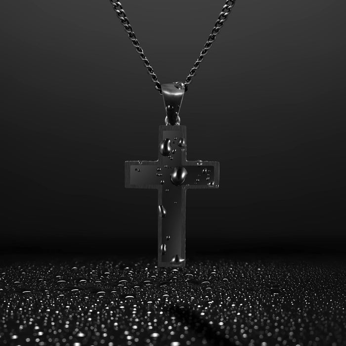 Close-up of a black cross pendant with a black chain, with water droplets on the pendant.