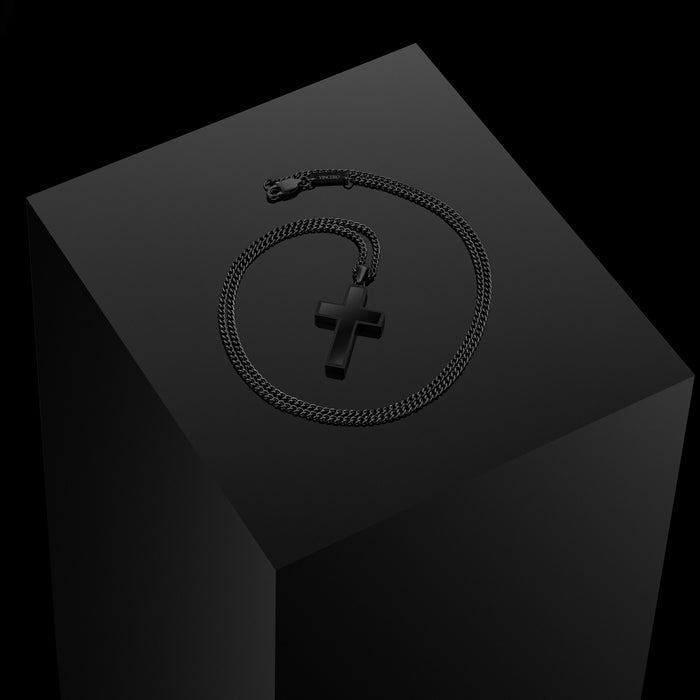 Black cross pendant with a black chain, displayed on a black podium.