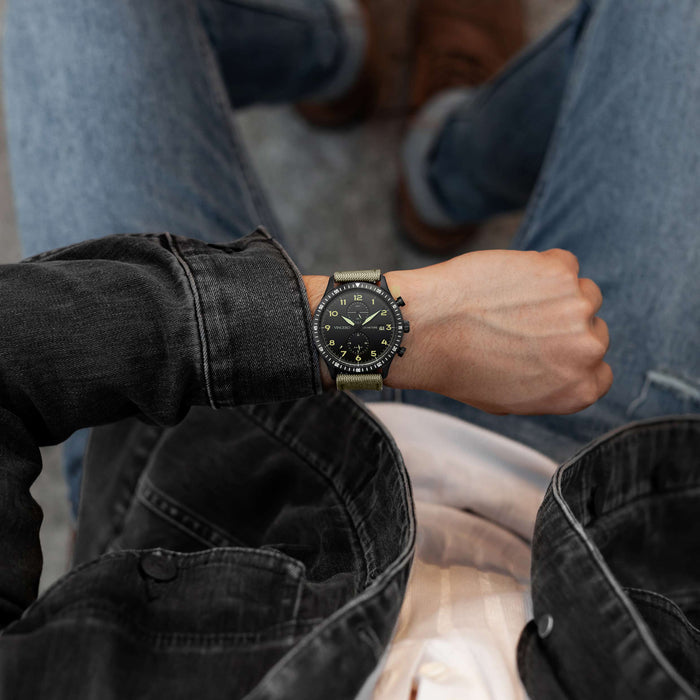 Person wearing a black watch with a detailed face, sitting on a bench.