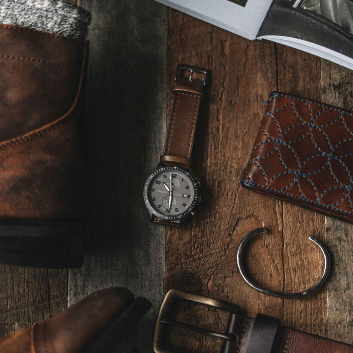 Brown leather boots, watch, wallet, and belt on a wooden surface