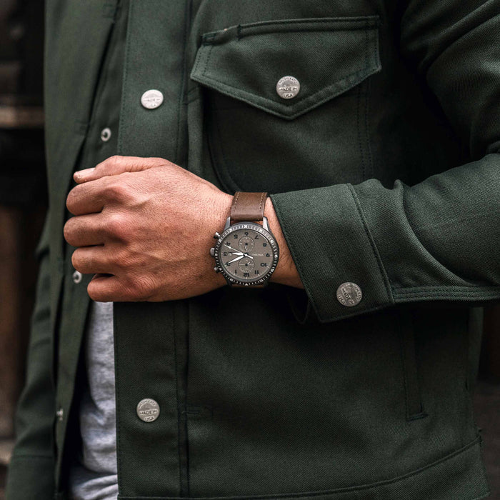 Person wearing a dark green jacket with a watch on their wrist.