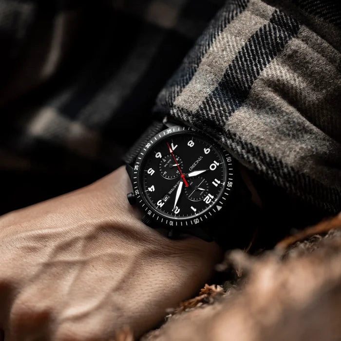 Black wristwatch on a person's wrist with a checkered sleeve in a natural setting