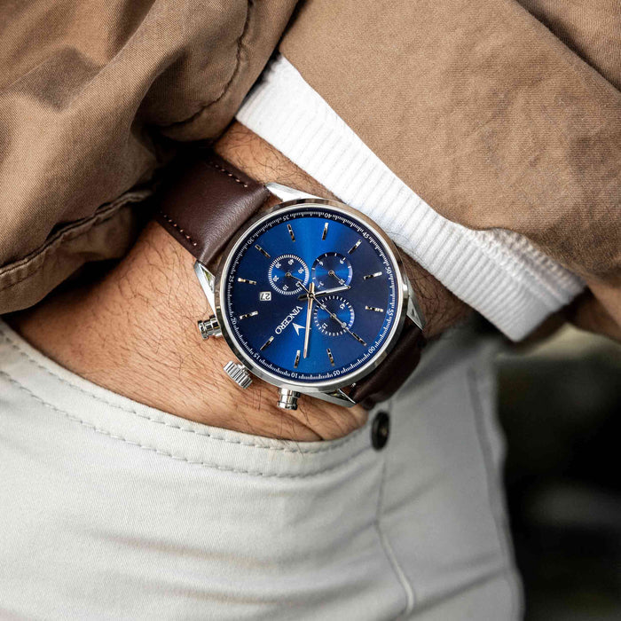 Close-up of a person wearing a watch with a blue face and brown leather strap.