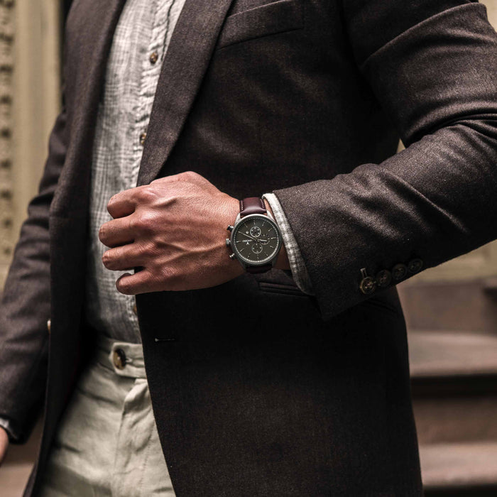Person wearing a dark coat and a watch, with a blurred background