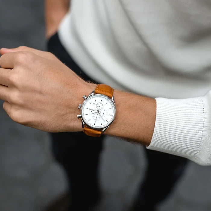 Person wearing a watch with a brown leather strap on a blurred background
