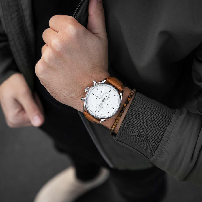 Hand wearing a watch with a brown leather strap on a dark background