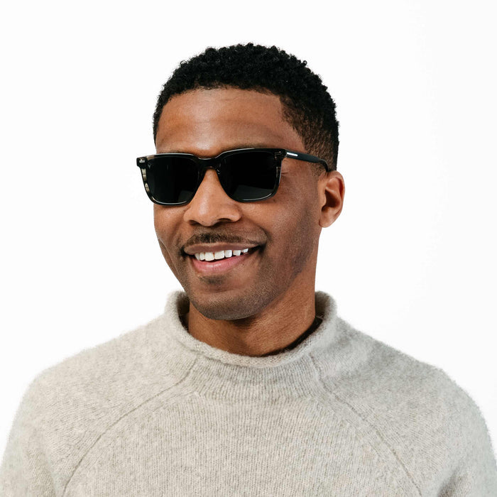 Man wearing sunglasses and a light gray sweater on a white background
