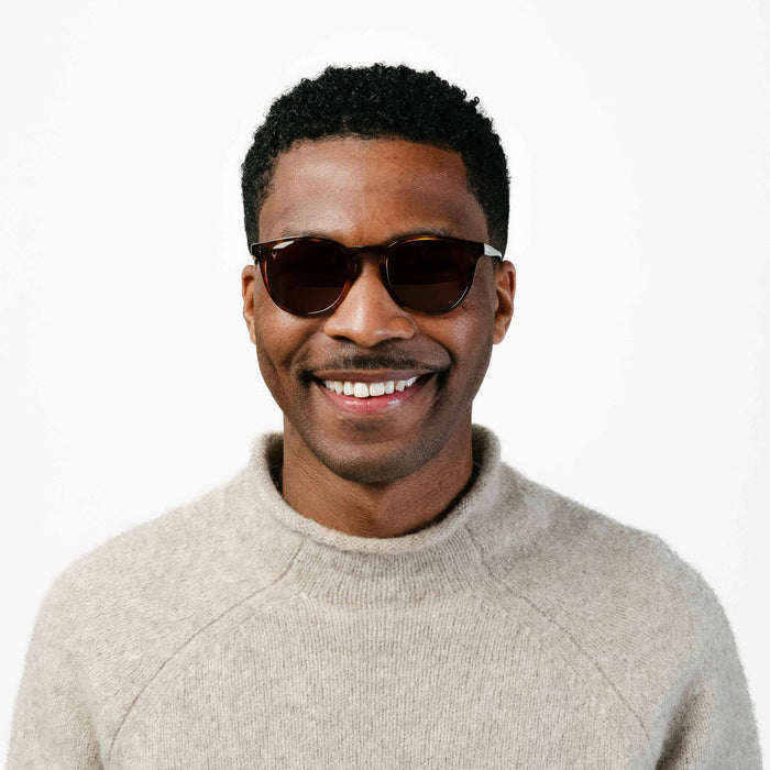 Man wearing sunglasses and a light gray sweater on a white background