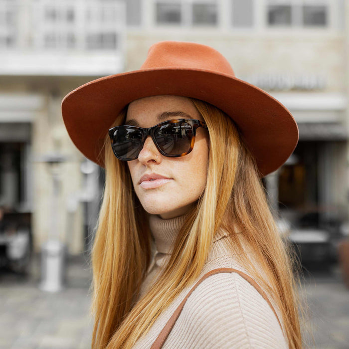 Woman wearing a brown hat and sunglasses on a city street