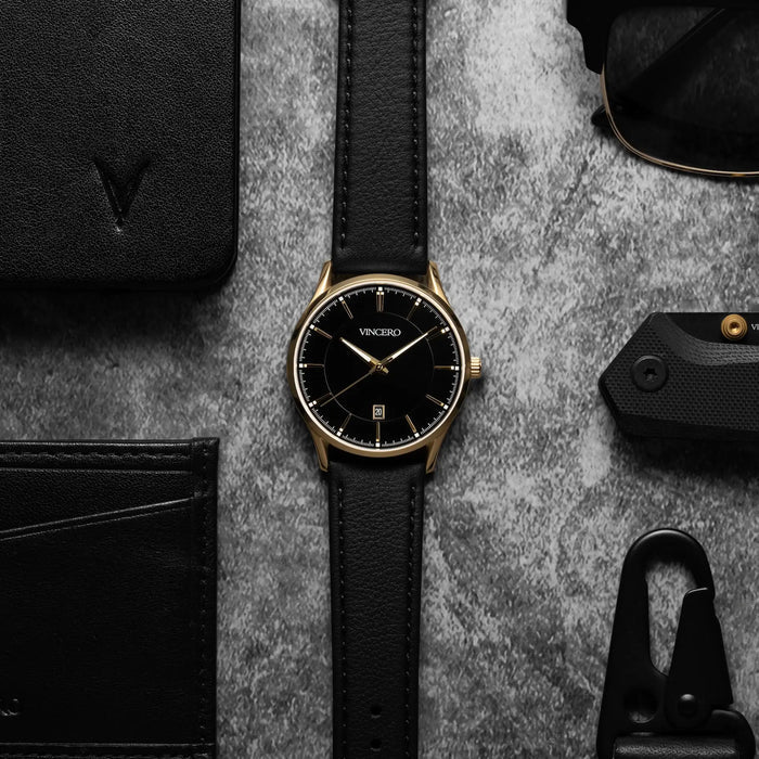Black watch with gold accents on a gray surface with accessories