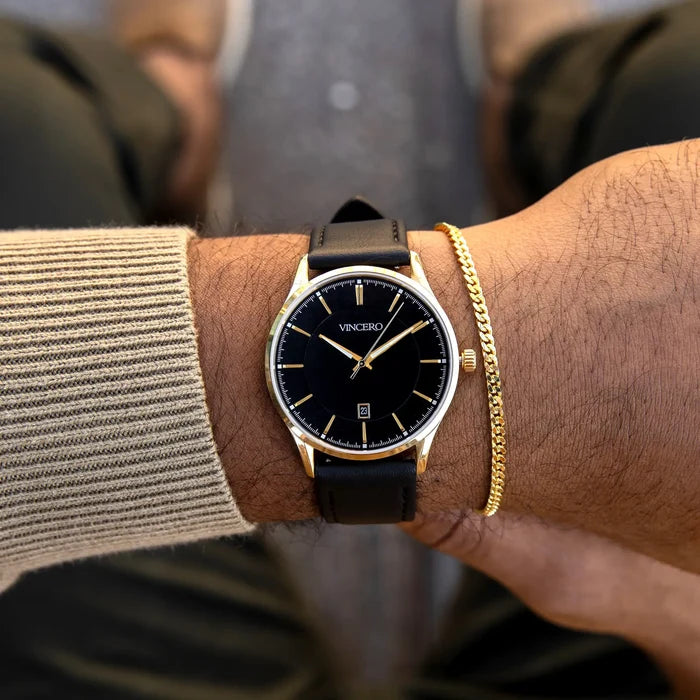 Black wristwatch with gold accents on a person's wrist, wearing a gold bracelet.