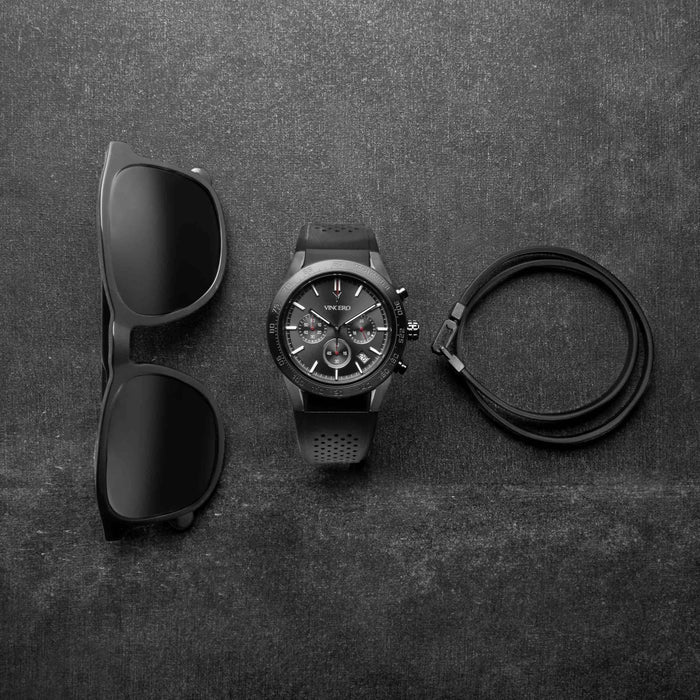 Black sunglasses, watch, and lanyard on a dark textured surface