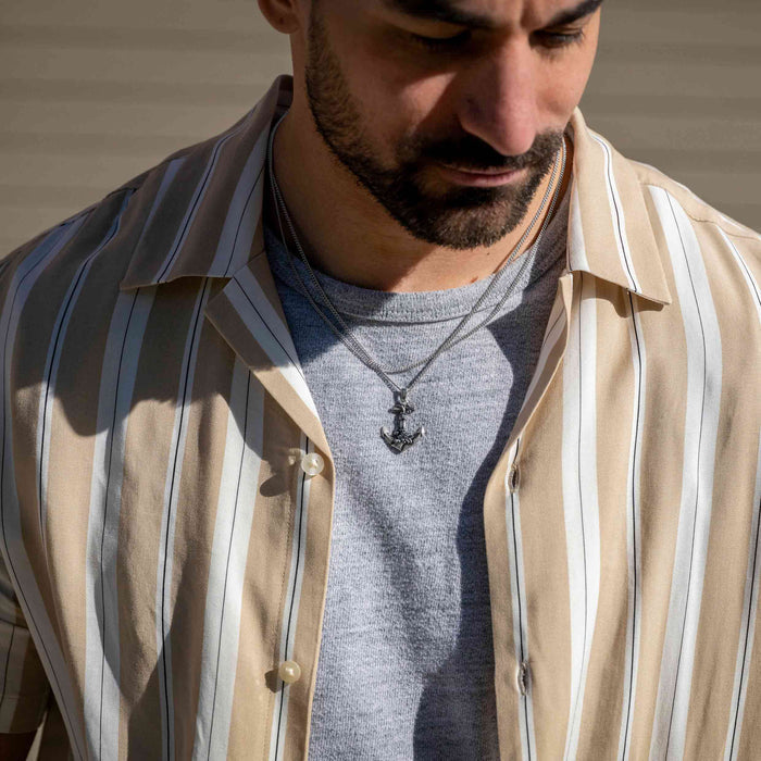 Man wearing a striped shirt over a gray t-shirt with an anchor necklace.