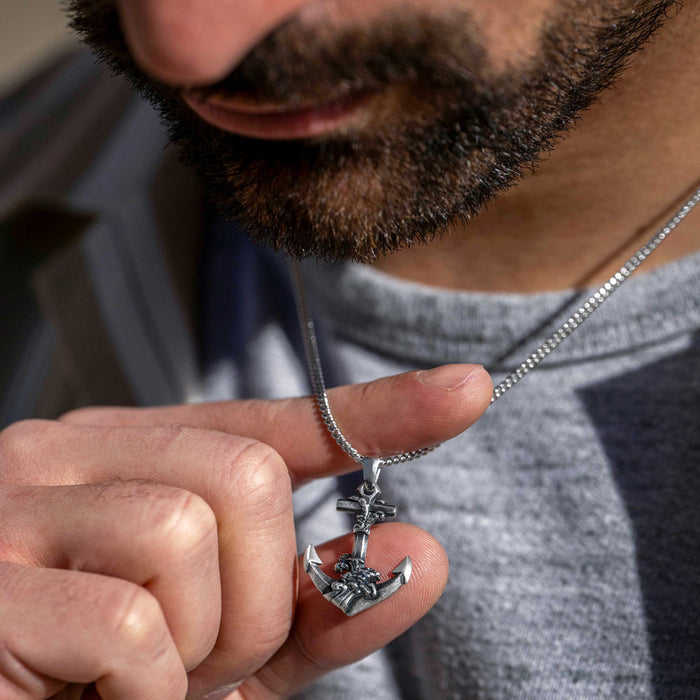 Man holding a silver necklace with a pendant close to his face