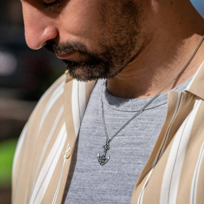 Man wearing a necklace with an anchor pendant, outdoors.