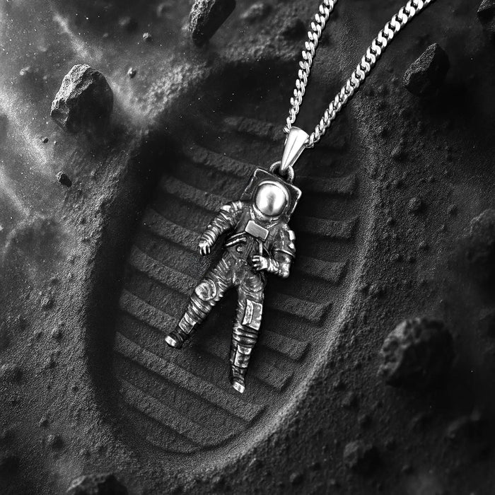 Astronaut pendant necklace on a textured surface resembling the moon's surface.