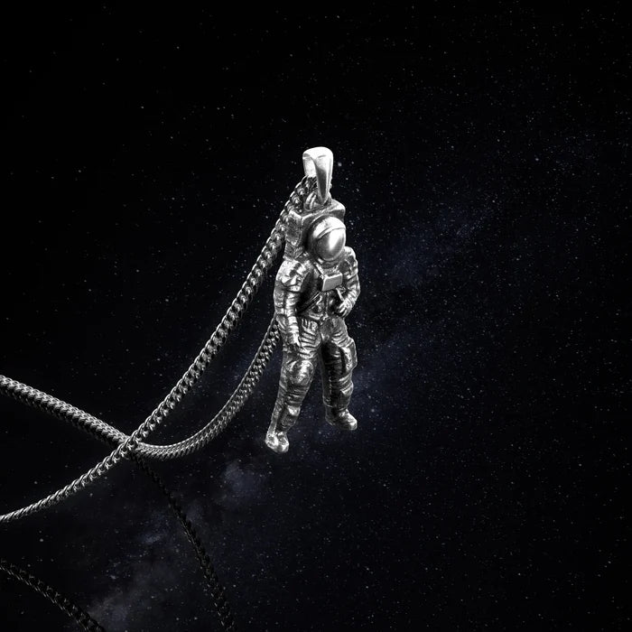 Silver astronaut pendant on a chain against a black background