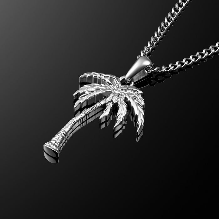 A silver-toned stainless steel necklace featuring a detailed palm tree pendant, shown against a dark gradient background.