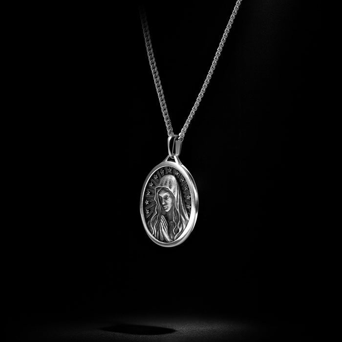 Silver pendant necklace with a religious design on a black background