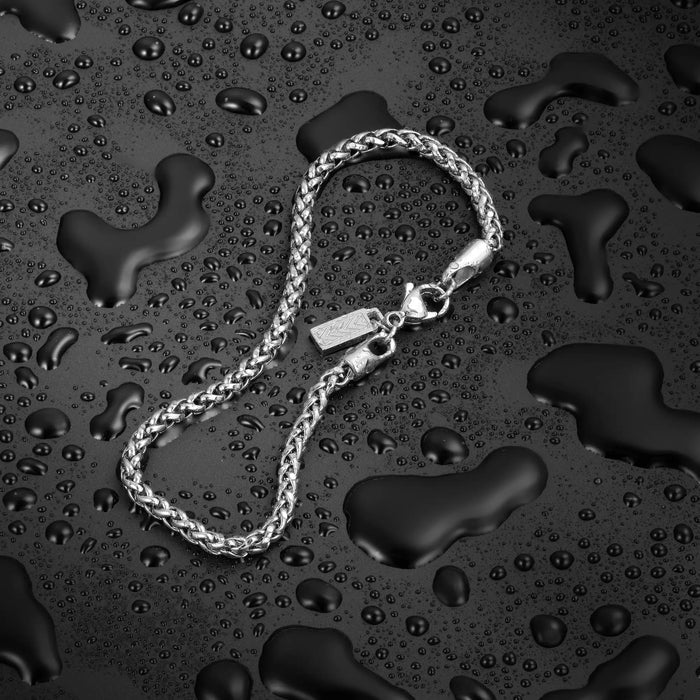 Silver chain bracelet on a textured black surface with water droplets