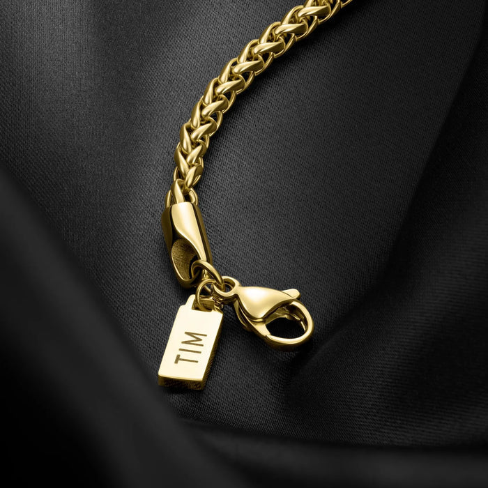 Gold chain bracelet with a 'TIM' tag on a black fabric background