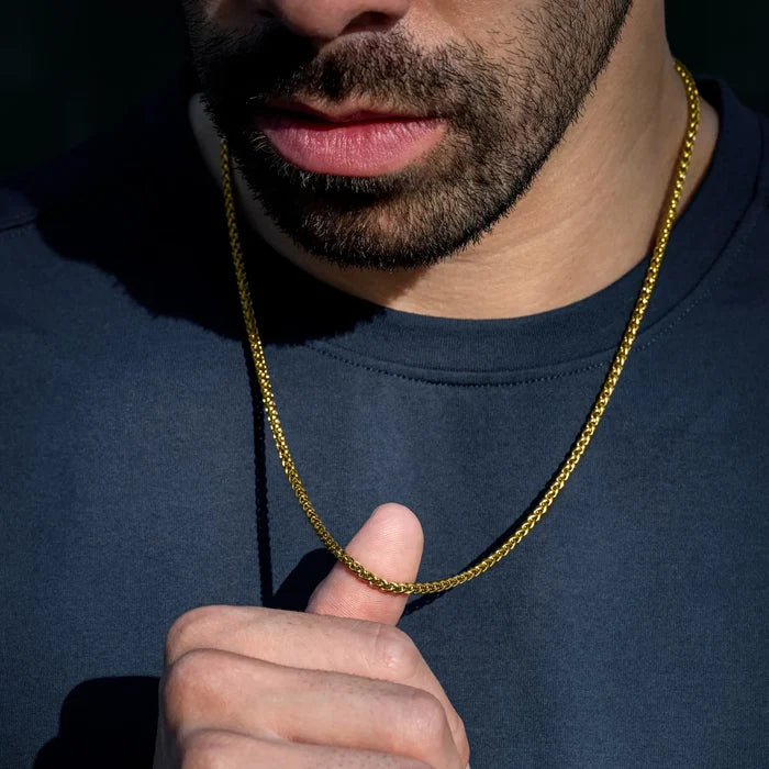 Man wearing a gold chain necklace against a dark background