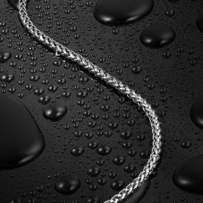 Silver braided necklace on a black surface with water droplets
