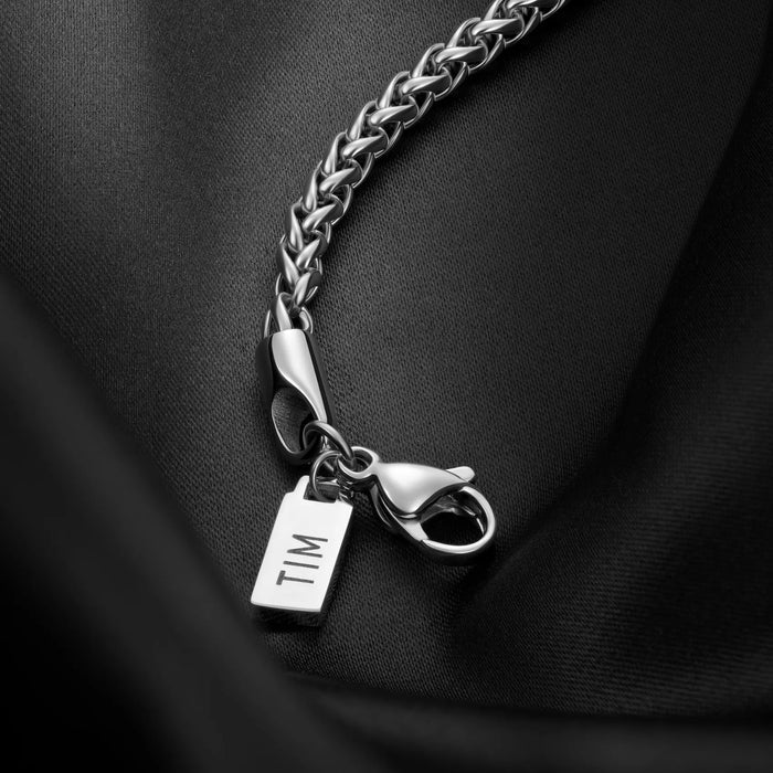 Silver chain bracelet with a tag and pendant on a black fabric background
