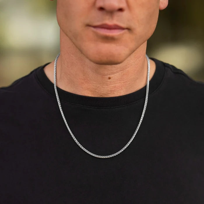 Man wearing a silver chain necklace against a blurred background